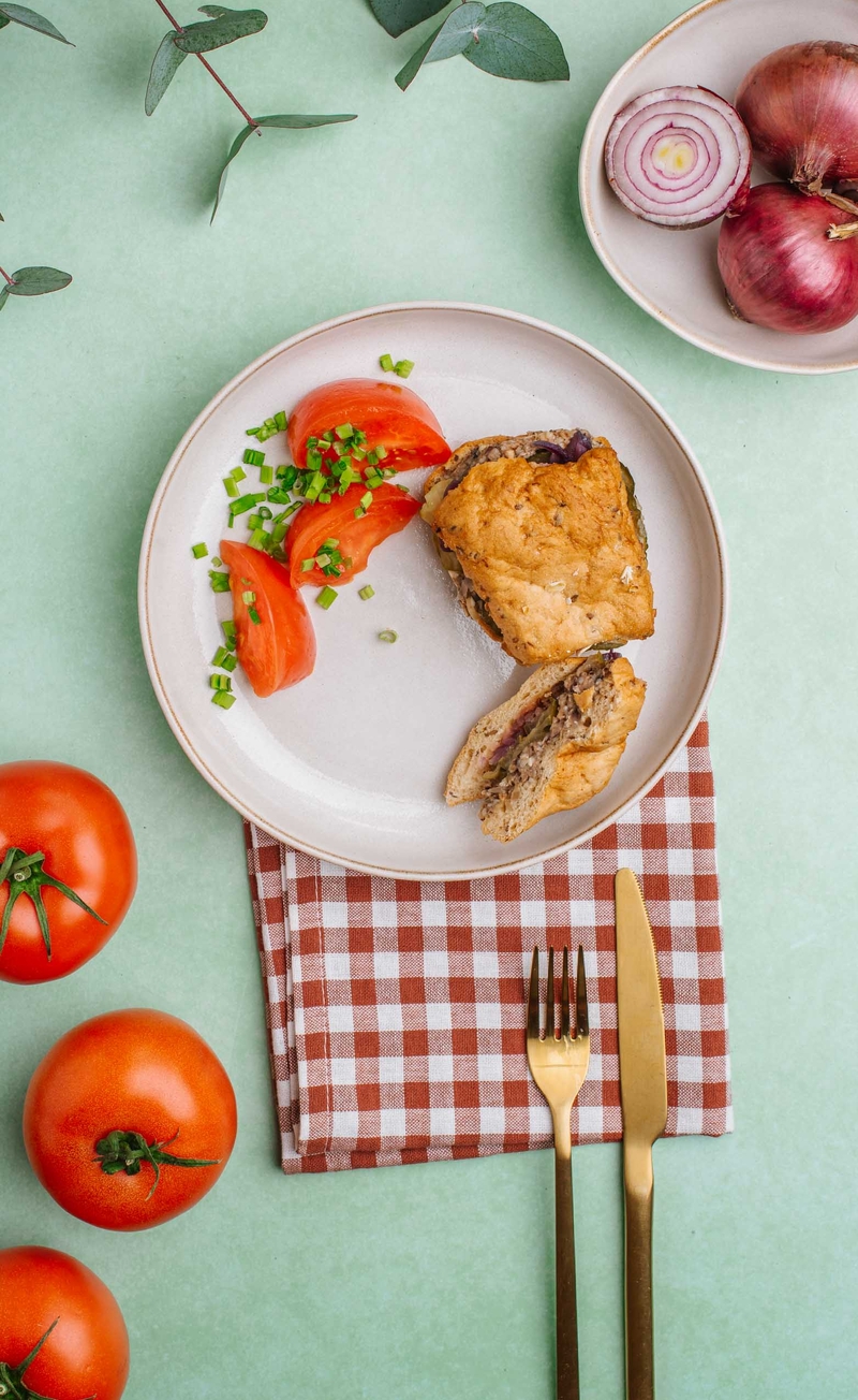 Burger owsiany z roślinną kaszanką, ogórkiem konserwowym i marynowaną czerwoną cebulką, pomidor ze szczypiorkiem