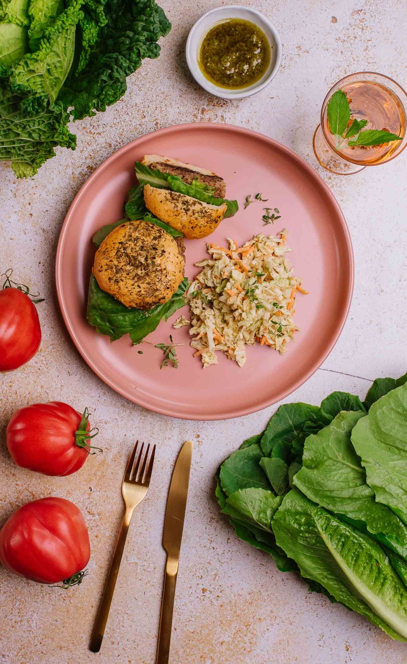 Burger z czarnej fasoli w pomidorowej bułce z piklowaną cebulą, sałatą lodową i pomidorem, salsa verde, colesław z włoskiej kapusty