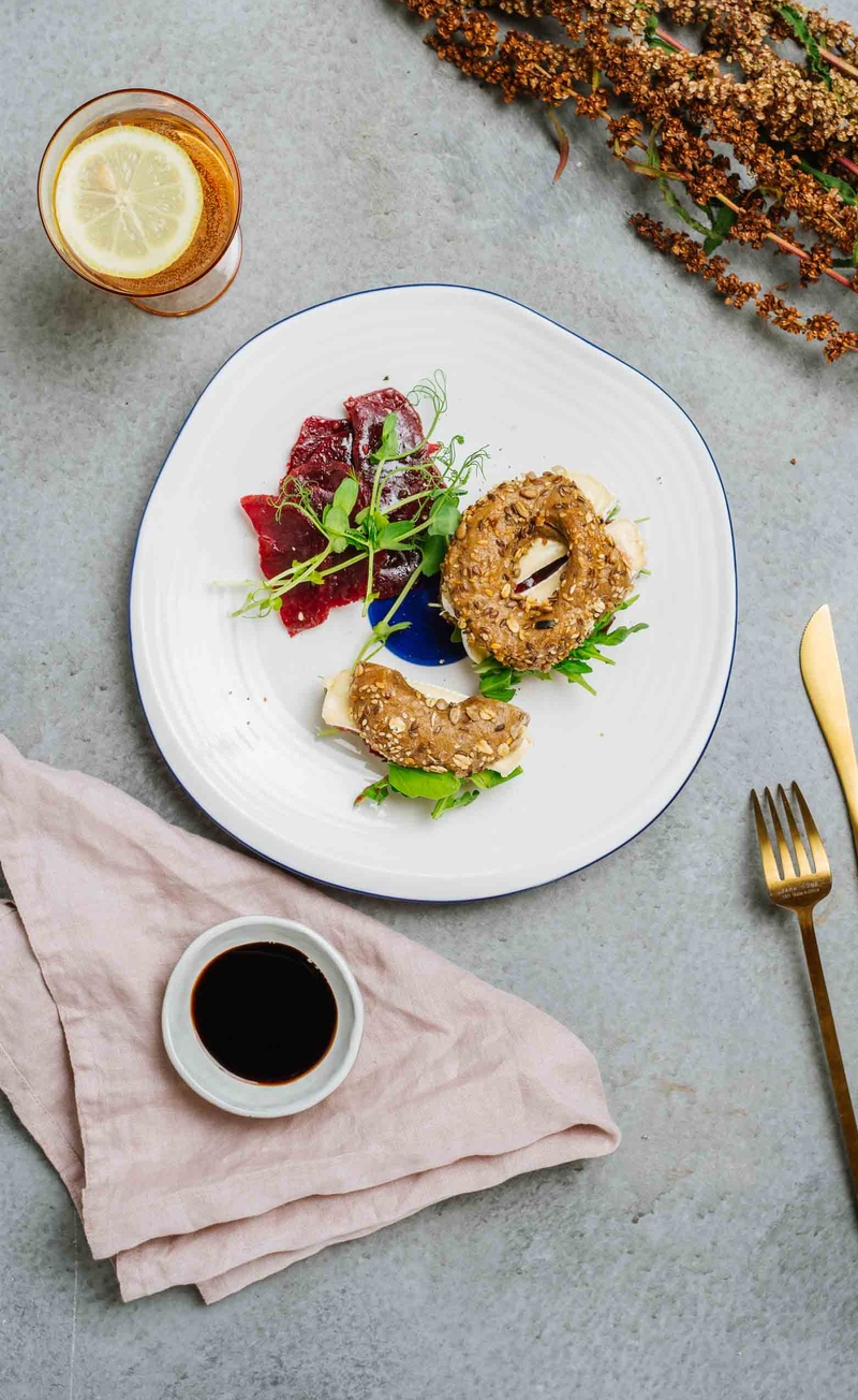 Bajgiel z ziarnami z konfiturą żurawinową, serem camembert i rukolą, carpaccio z buraka, krem balsamiczny