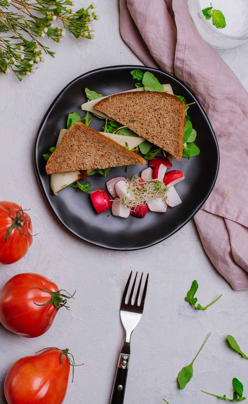 Kanapka razowa z pomidorowym pesto, rukolą i żółtym serem, cząstki rzodkiewki