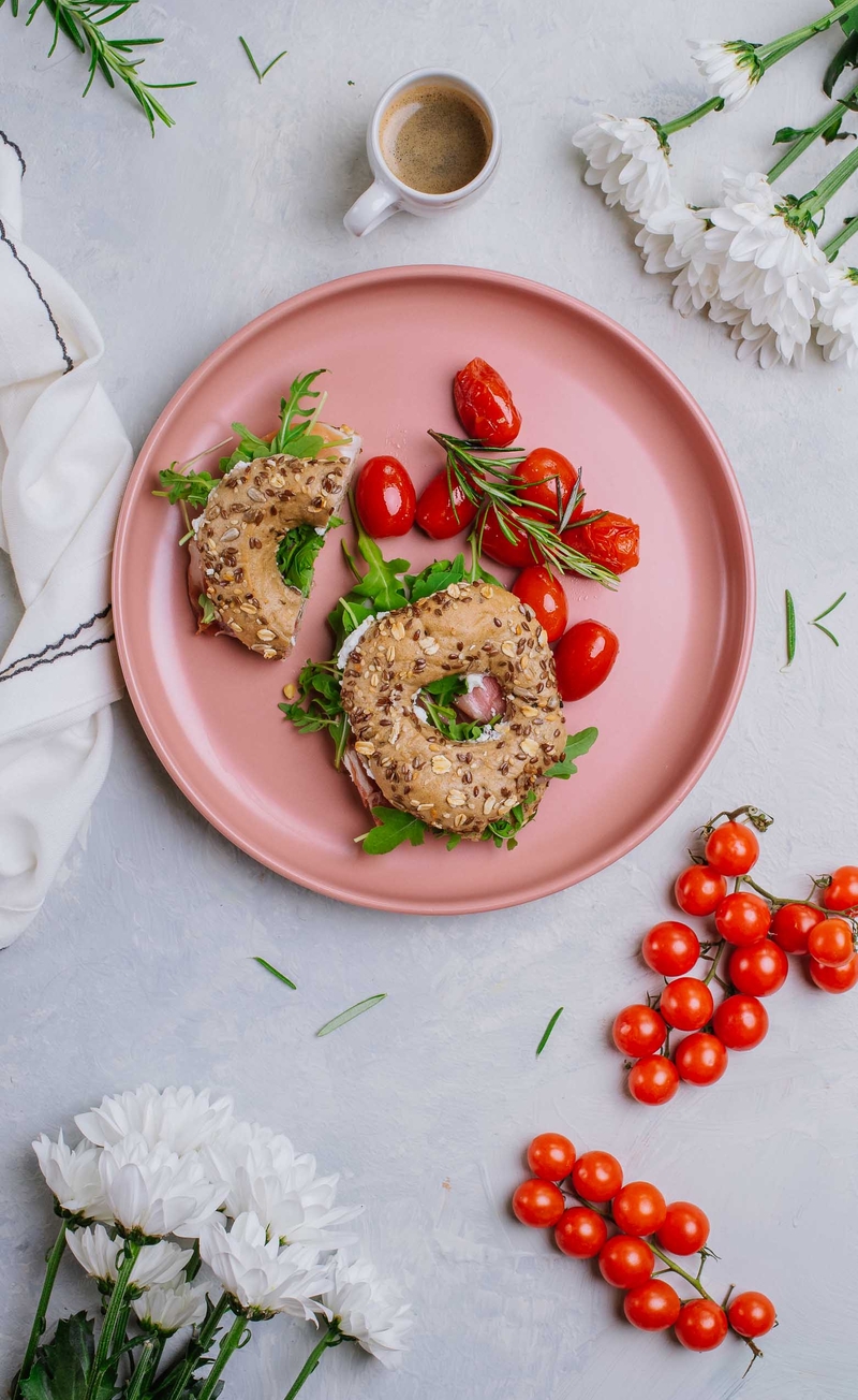 Bajgiel z ricottą, szynką dojrzewającą, prażonymi orzechami pinii i rukolą, pieczone pomidorki w kremie balsamicznym