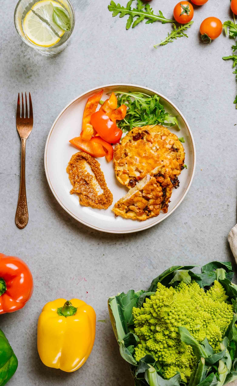 Keto pizza na kalafiorowym spodzie z kiszoną kapustą i boczkiem, pesto pomidorowe, świeże warzywa