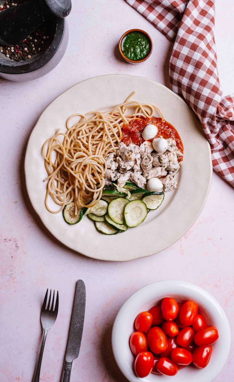 Makaron razowy z kawałkami kurczaka w sosie pomidorowym z mini mozzarellą, plastry cukinii z pesto bazyliowym