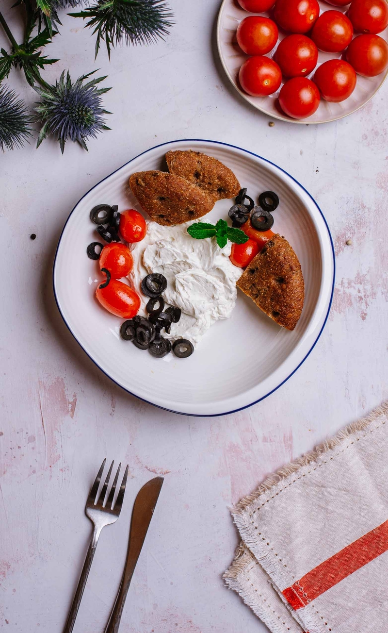 Labneh z pieczonymi pomidorkami w paście harissa i oliwkami, żytni podpłomyk