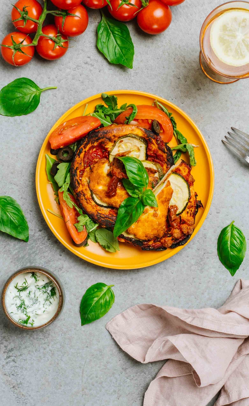 Śródziemnomorska mini pizza z halloumi, cukinią i suszonymi pomidorami, sos tzatziki, pomidory z oliwkami i rukolą