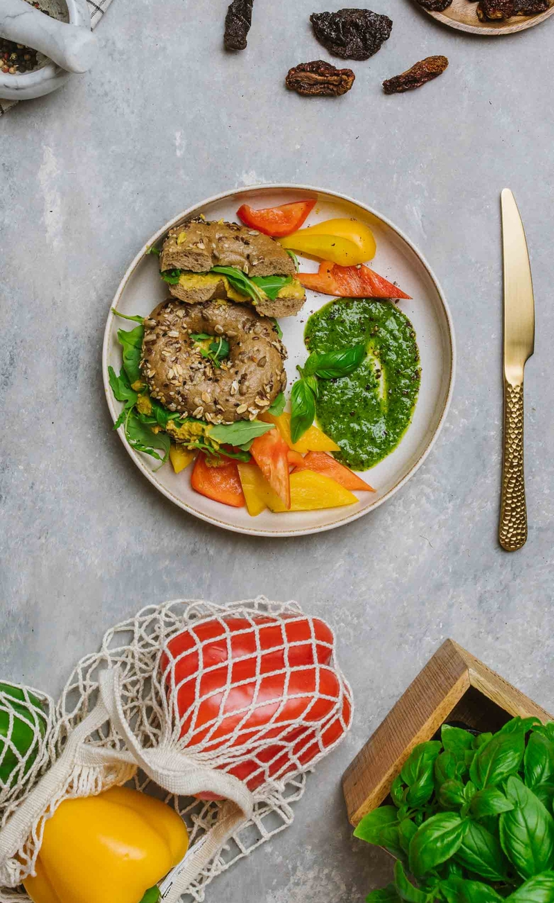 Bajgiel z bezjajeczną pastą z suszonymi pomidorami i rukolą, papryka, pesto bazyliowe
