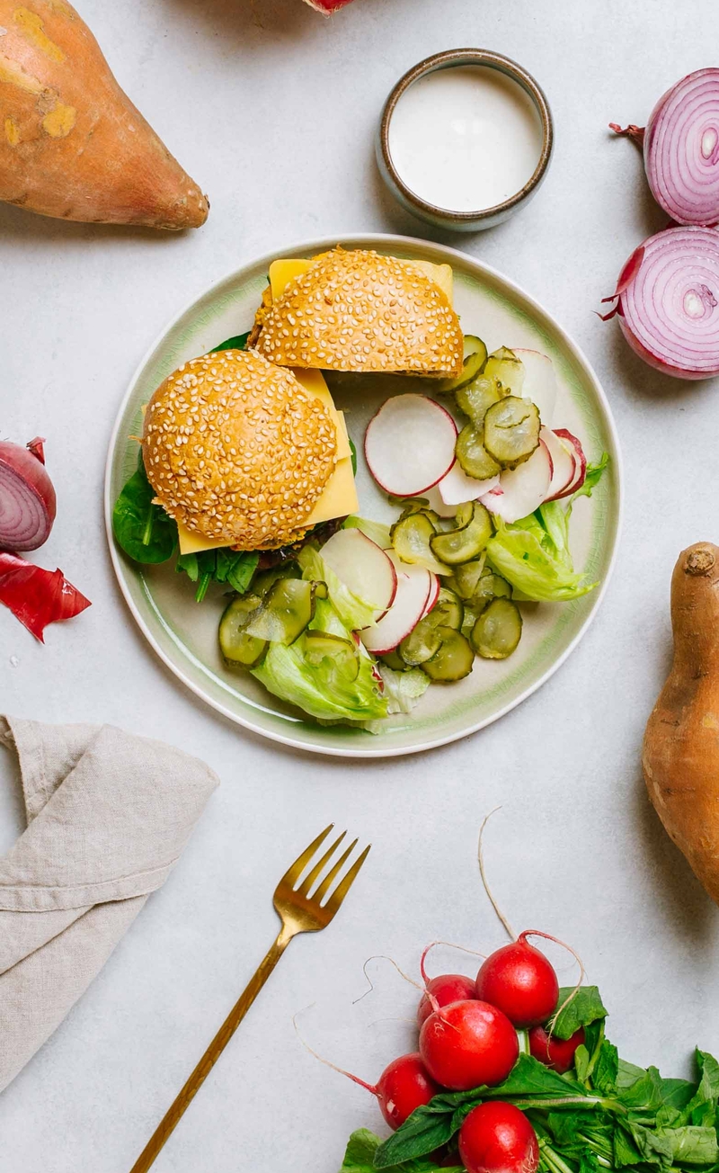 Burger z batata i ciecierzycy z czerwoną cebulą w bułce z sezamem, sałata lodowa z ogórkiem kiszonym i rzodkiewką