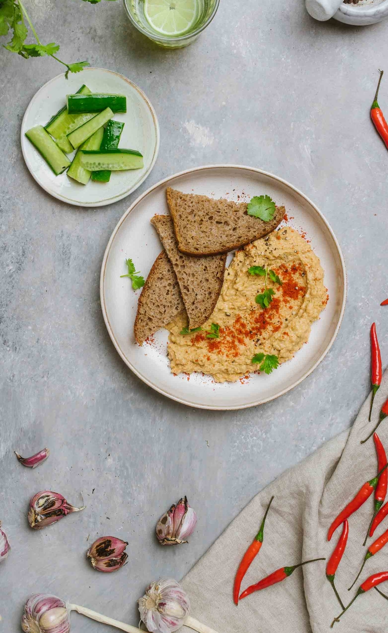 Hummus z pieczonym czosnkiem i harrisą, chleb razowy, ogórek zielony